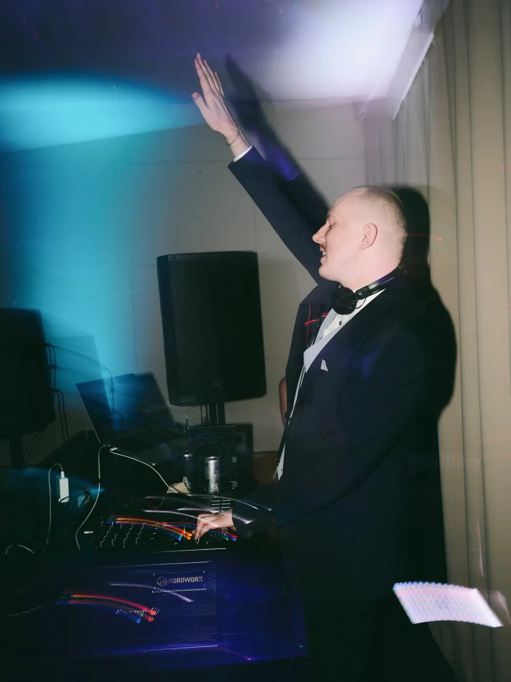 Max (WMAX) im Anzug am DJ-Pult, ein Arm in die Luft gestreckt